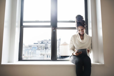 Smiling businesswoman using digital tablet while sitting at window