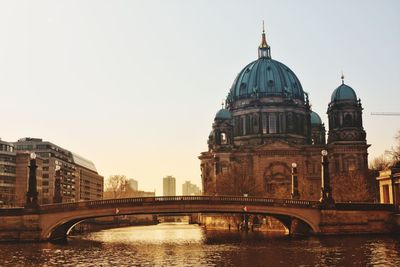 Arch bridge over river amidst buildings against clear sky