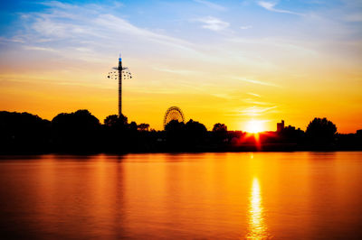 Silhouette trees by lake against orange sky