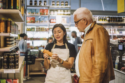 Saleswoman discussing over product with senior male customer at delicatessen