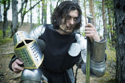 Knight holding sword and helmet in forest