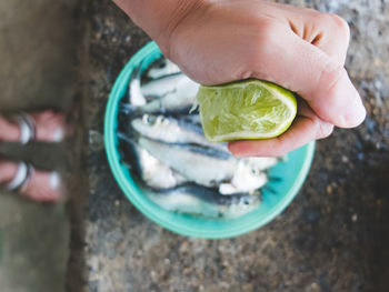 Cropped image of hand squeezing lemon on fish in container