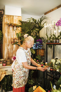 Blond female florist arranging plant on display rack in flower shop