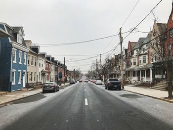 Cars on road by buildings in city against sky