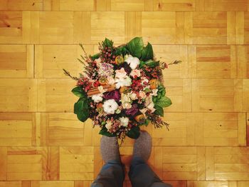 Low section of person standing by bouquet on hardwood floor