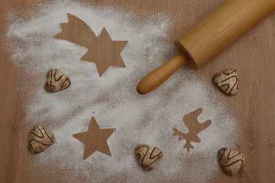 High angle view of cookies, flour and rolling pin on wooden background