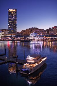 Boats moored in river by illuminated buildings against clear sky at night