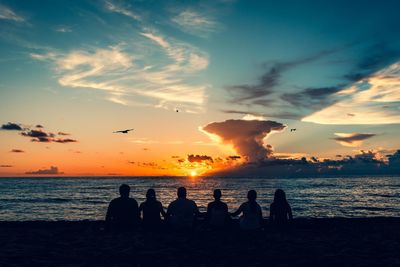 Silhouette people on beach against sky during sunset