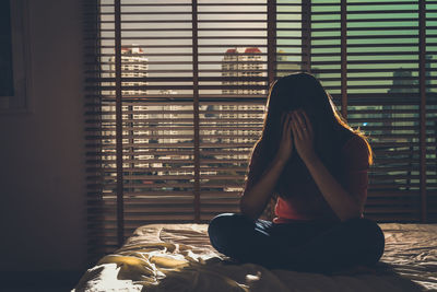 Rear view of woman sitting on bed at home