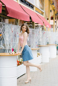 Cute young woman in a denim skirt and pink top stands near a metal white barrel on a walk 