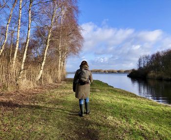 Rear view of woman walking over a footpath to a lake. trees at her left, at her right is a canal