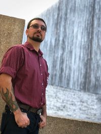 Confident man wearing sunglasses standing against waterfall