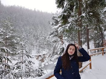 Portrait of young woman standing in forest during winter