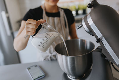 Mid section of woman pouring milk into stainless steel bowl