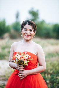 Young woman standing by red flower on field