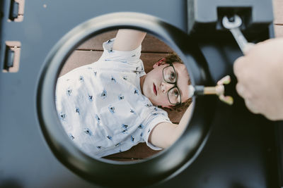 Overhead view of boy making metallic cabinet while lying on floorboard at porch