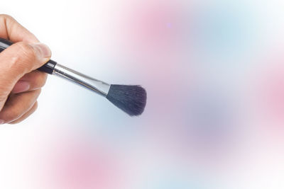 Cropped hand holding make-up brush against colored background