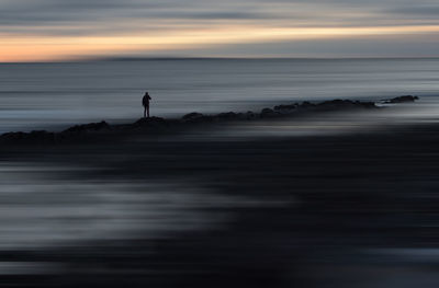 Silhouette person standing on beach against sky during sunset