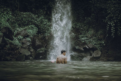 Full length of shirtless man splashing water in forest