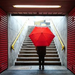 Rear view of woman with red umbrella standing in underground walkway