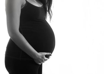 Midsection of pregnant woman with hands on stomach standing against white background