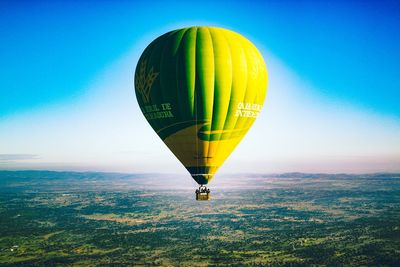 Hot air balloon flying over landscape against blue sky
