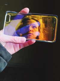 Reflection of young woman on phone cover against black background