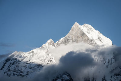 Low angle view of snowcapped mountains against clear blue sky