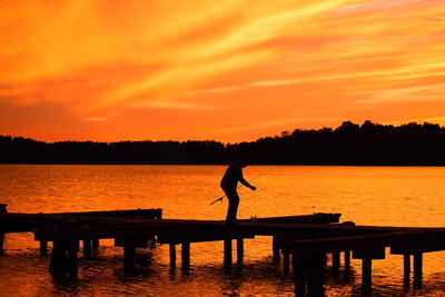 Silhouette man standing by lake against orange sky