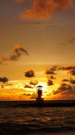 Silhouette built structure by sea against orange sky