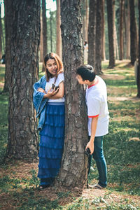 Full length of young woman standing by tree trunk in forest