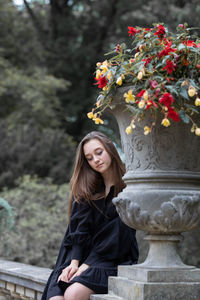 Beautiful young woman sitting by sculpture at park