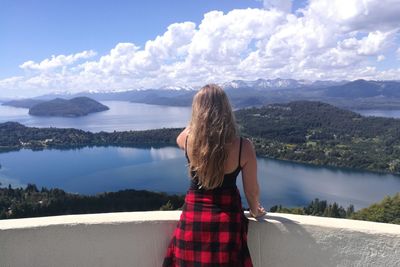 Rear view of woman standing by lake against sky