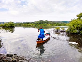 Rear view of man sitting in lake against sky