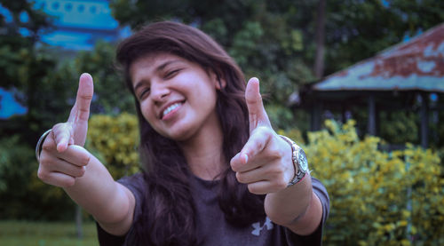 Portrait of smiling young woman gesturing while standing against plants