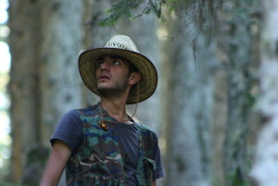 Portrait of man wearing hat standing against trees in forest