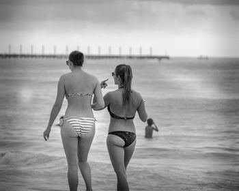 Rear view of friends enjoying at beach against sky