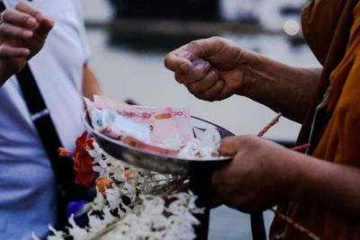 Midsection of monk with paper currency in plate standing by man 