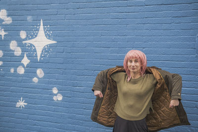 Smiling punk woman wearing jacket in front of blue wall