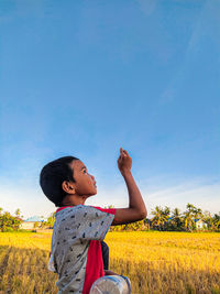 Boy looking away while standing on field against sky