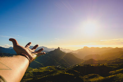 Cropped image of hand against mountain during sunset