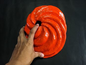 Close-up of hand holding red chili pepper against black background