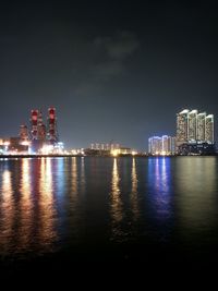 Illuminated city by sea against sky at night