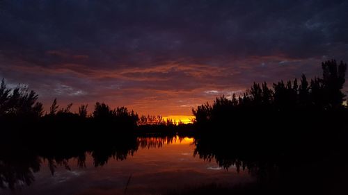 Silhouette trees by lake against sky at sunset