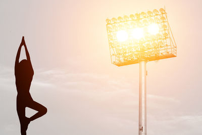 Silhouette woman practicing tree pose against illuminated floodlight