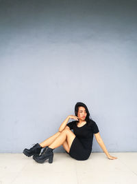 Young woman looking away sitting against wall