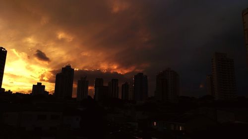 Silhouette of city against dramatic sky during sunset