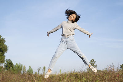 Young woman with arms raised on field against sky