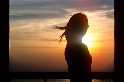 Silhouette woman standing against orange sky