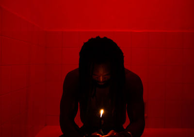 Man holding burning candle while sitting in bathroom